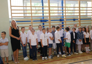 Nauczyciele i uczniowie w czasie uroczystości na sali gimnastycznej