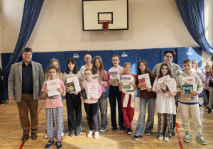 Grupa nauczycieli i uczniów z dyplomami na sali gimnastycznej