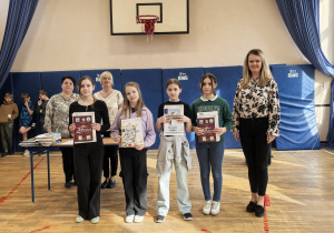 Grupa nauczycieli i uczniów z dyplomami na sali gimnastycznej