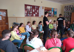 Uczniowie klasy IV a siedzą na krzesłach słuchają informacji przekazywanych przez Szymona i Borysa.