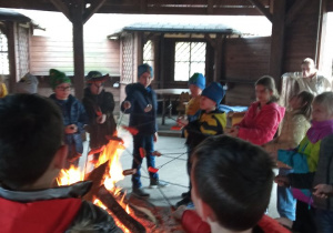 Dzieci piekące kiełbaski przy ognisku.