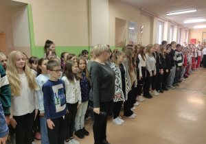 Uczniowie śpiewający hymn państwowy na korytarzu szkoły.