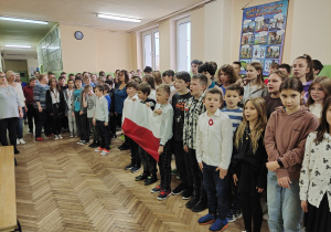 Uczniowie śpiewający hymn państwowy na korytarzu szkoły.